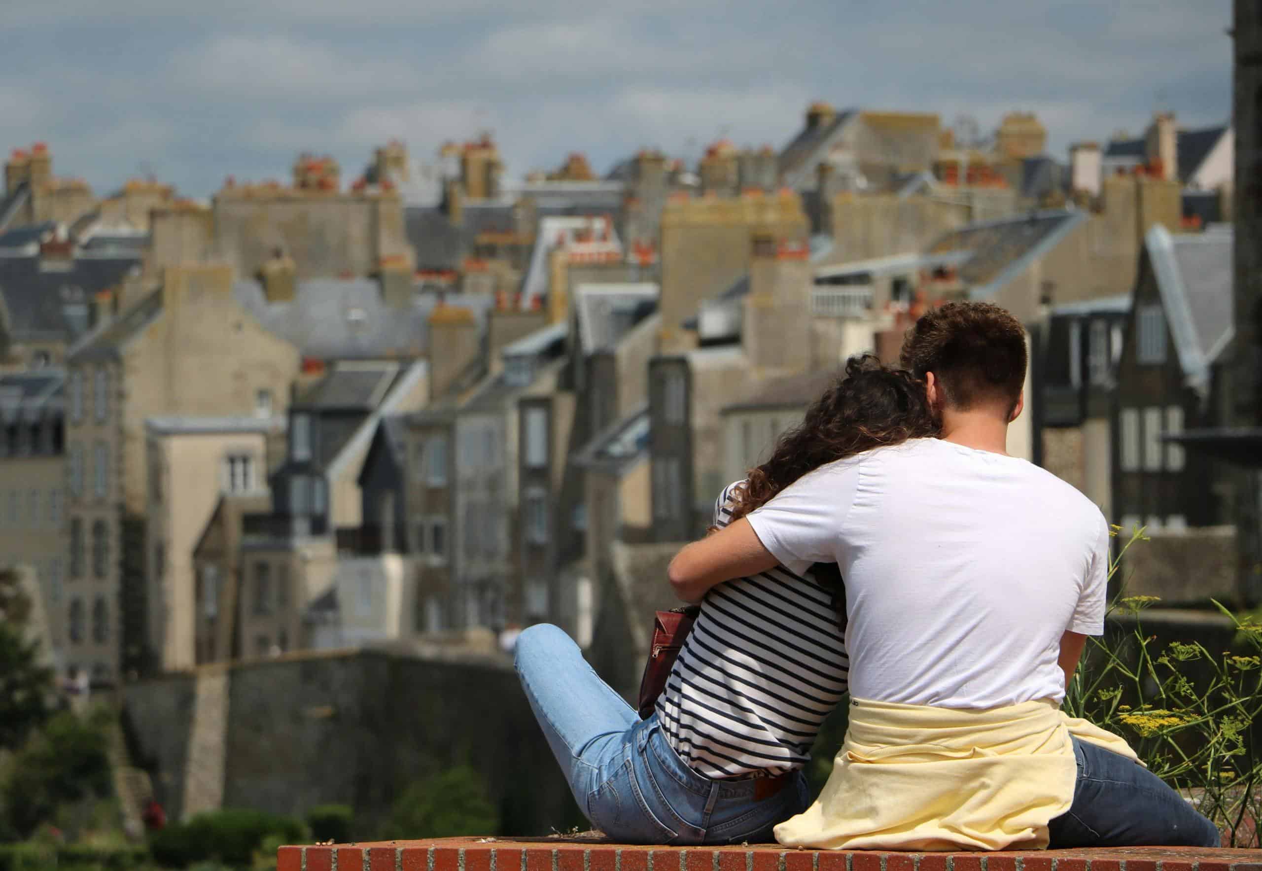 A couple embraces while sitting outdoors overlooking the Granville cityscape in Normandy, France.